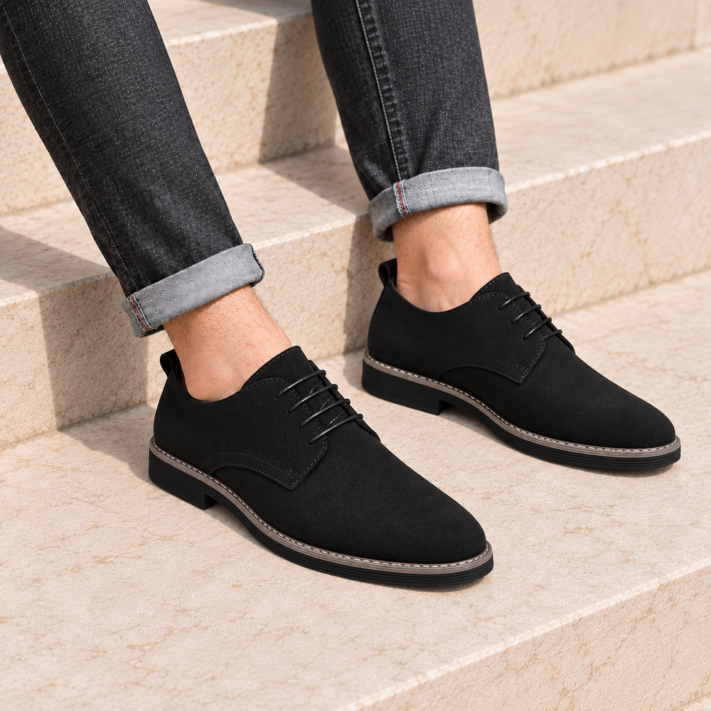 Black suede derby shoes worn with cuffed charcoal jeans on stone